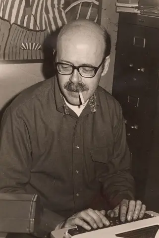 Black and white photo of person typing with cigarette in mouth.