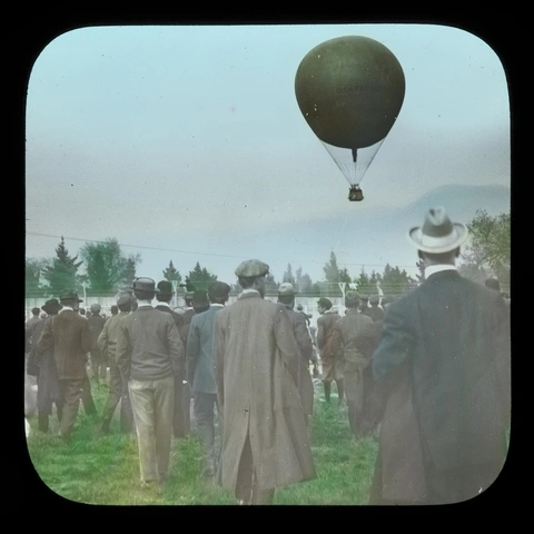 A group of people watch a hot air balloon rise into a clear sky.