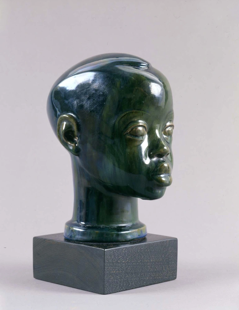 Three-quarter profile view of a small blue/green glazed terracotta sculpture of a young Black boy's head and neck.