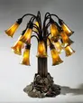 Lamp with rounded metal decorative leaves at the base and eighteen orange glass bulb covers in the shape of lily flowers.