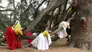 Black and brown people wearing red, yellow, and white drape their bodies over the branches of a large tree.