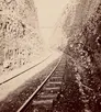 Faded black and white photo of train tracks running through a narrow canyon.