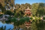 A Chinese-style garden with a tiered-tower structure surrounded by trees and shrubs, reflecting in a large body of water.