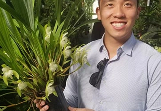 A smiling person holds a potted orchid.