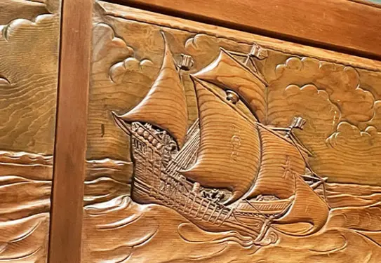 A detail view of a carved wood panel depicting a ship at sea.