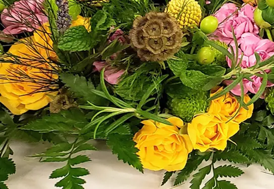 A floral arrangement with yellow and pink roses and green herbs.