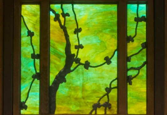 A green stained glass window with floral designs in a dark wood frame.