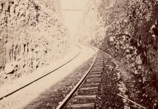 Faded black and white photo of train tracks running through a narrow canyon.