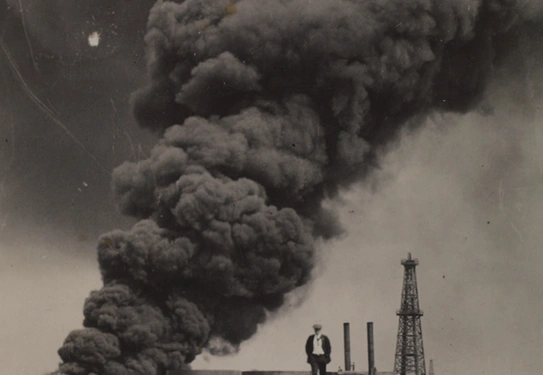 A black and white image of a smoke cloud rising from the ground with a person walking away.