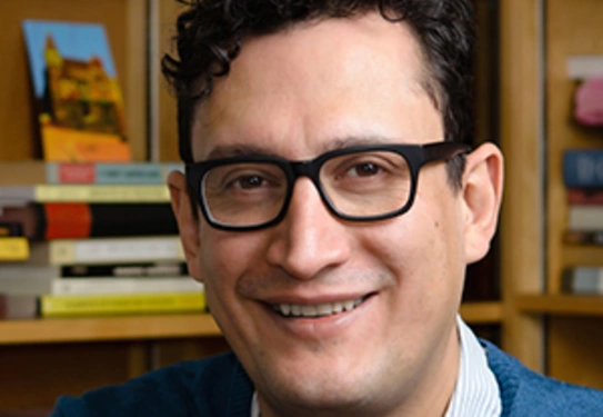 Pablo F. Gómez poses for headshot taken in front a bookshelf.