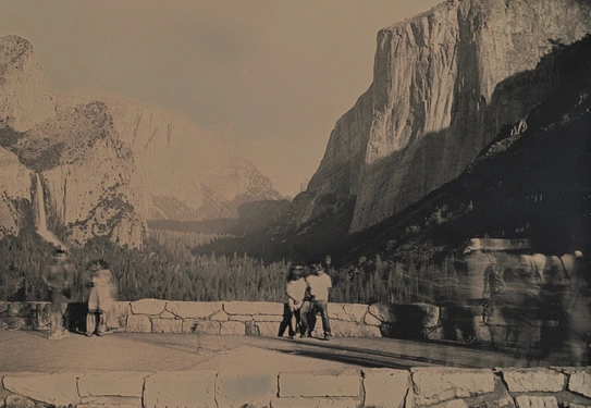 A grayscale image of people near a paved road in a national park with large mountains and a forested valley.