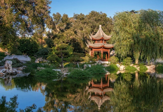 A Chinese-style garden with a tiered-tower structure surrounded by trees and shrubs, reflecting in a large body of water.