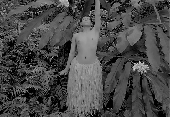 A person in a grass skirt stretches in a forest.