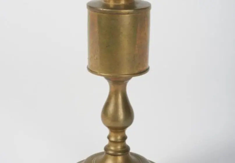 Brass lamp that resembles a large candlestick with a reservoir and two wick holders at the top in the shape of a V.