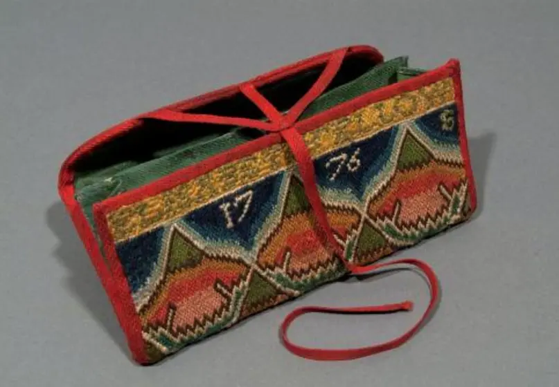Accordion-style wallet with foldover flap decorated throughout with geometric floral pattern in dominant shades of pink, blue and yellow with the words with “Elisabeth Fellows 1776” embedded in the design.