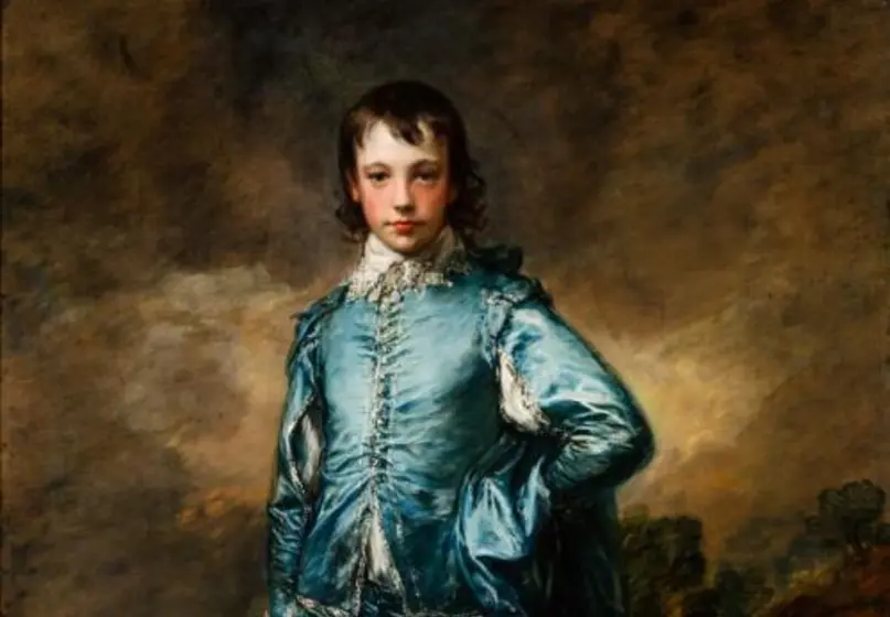 A full-length boy standing in a blue silky costume with a hand on his hip, his left leg forward, and a hat in his right hand set against a gray-brown background. 