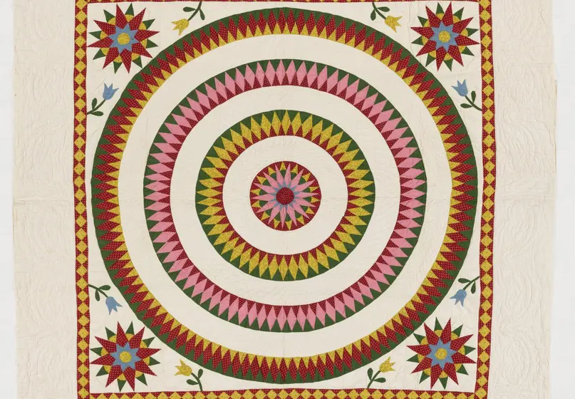 Image of a quilt with a large circle in the center and four concentric circles inside it with four star shaped images in each of the quilt's corners.