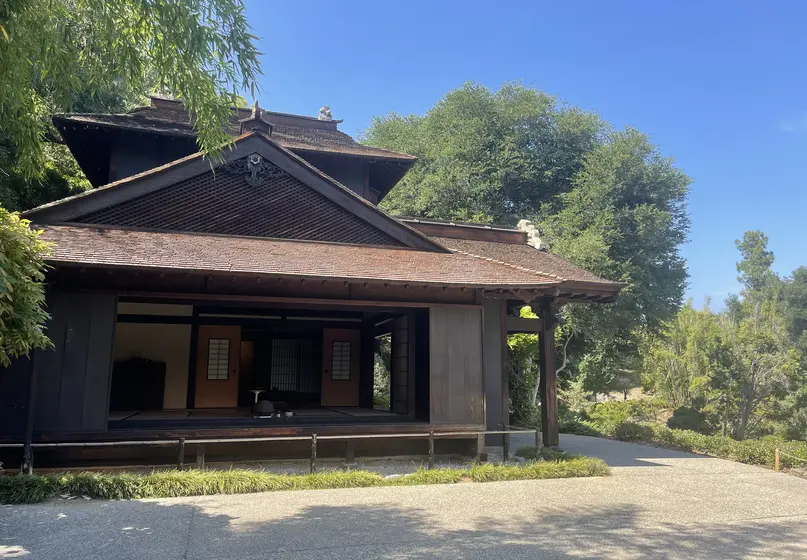 House-like structure with one wall open to display the interior. The house is surrounded by a paved open area and plants.