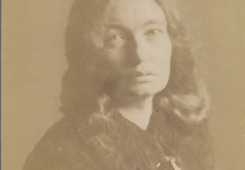 Sepia photograph of a person in their thirties or forties. The person has a serious expression and chest-length hair. They are wearing a longsleeve black shirt.
