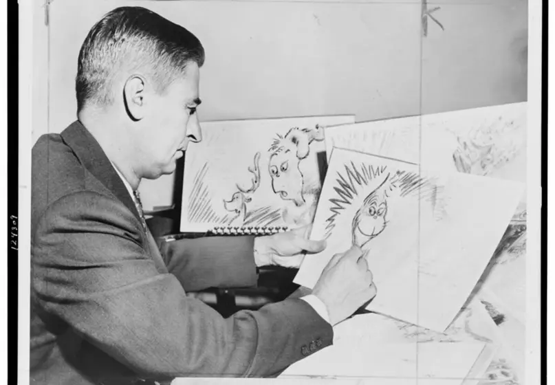 A man in a suit works on an illustration of the famous "Grinch" cartoon character.