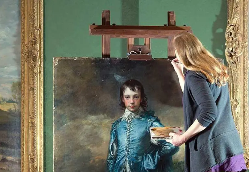 A Conservationist carefully touches up a tiny part of the painting "Blue Boy."