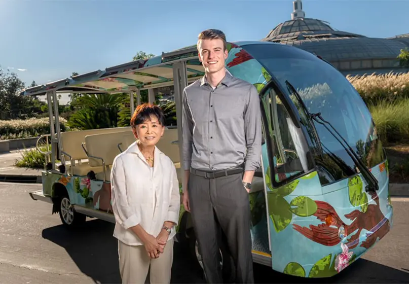 Two people stand in front of an electric passenger vehicle that's wrapped in a koi-inspired design.