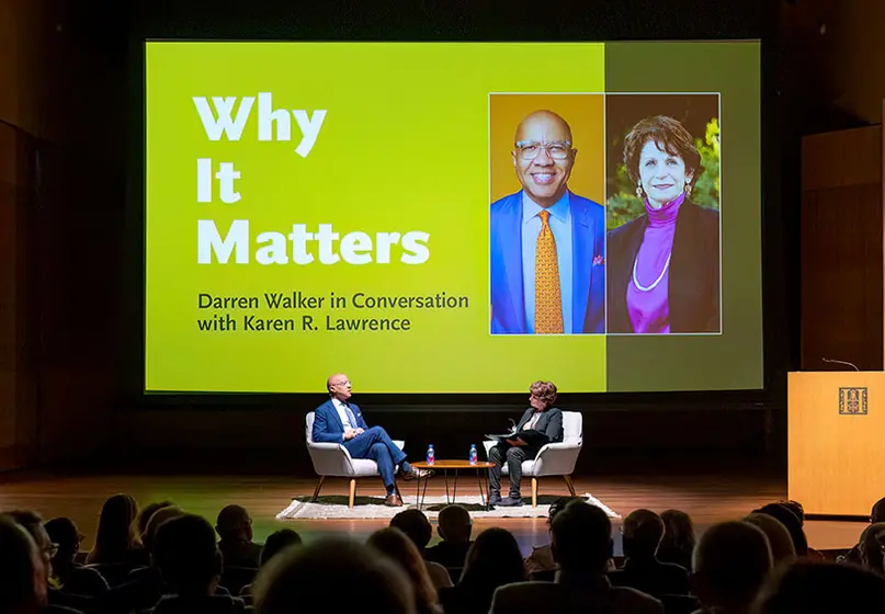An audience watches two people have a conversation on a stage, where a large graphic says, “Why It Matters.”