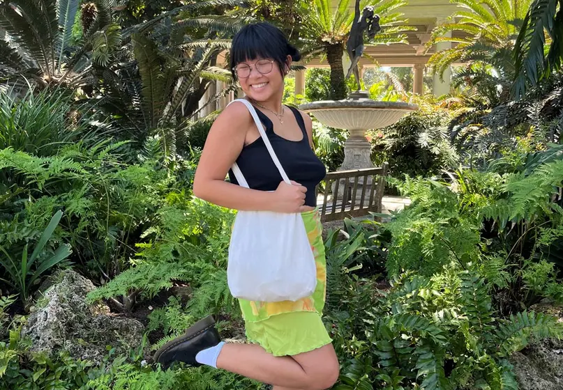 A college student poses near a fountain in a lush garden.