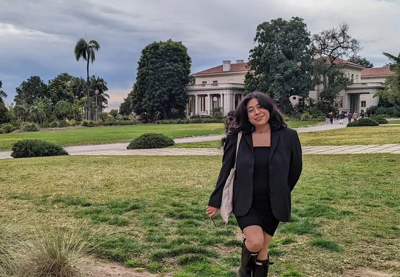 A college student walks across a lawn on a cloudy day. 