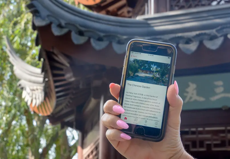 A person holds a phone in front of a traditional Chinese-style building.