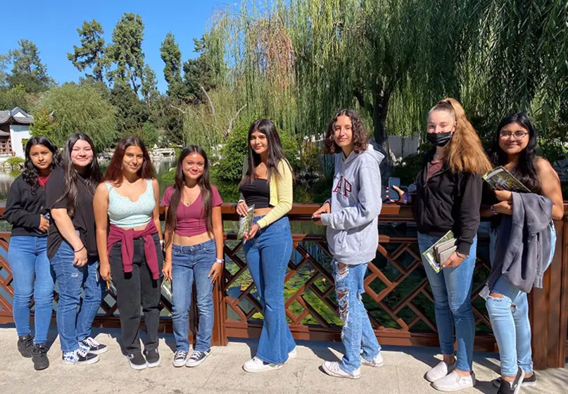 Several young people stand in front of a garden lake.