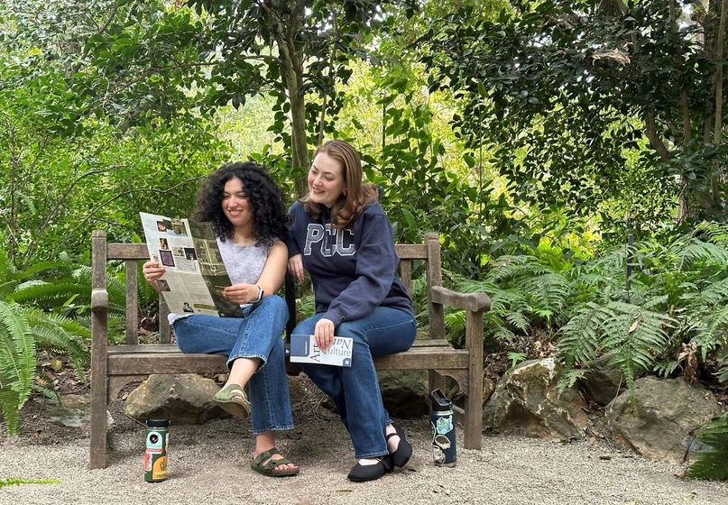 Two people sit on a bench in a garden, looking at a map.