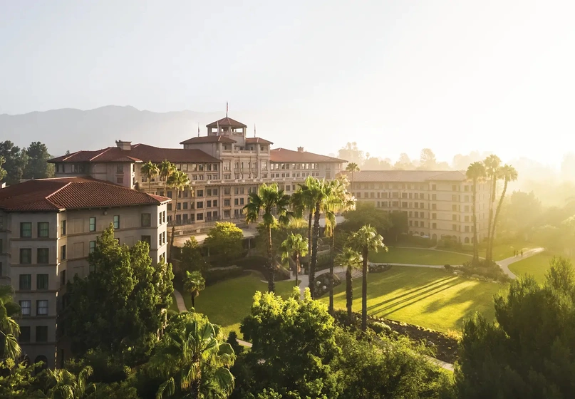 A large multi-story hotel surrounded by green lawns and lush gardens.