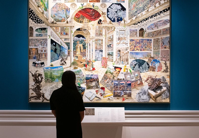 A person stands in a gallery with large-scale artworks on blue walls.