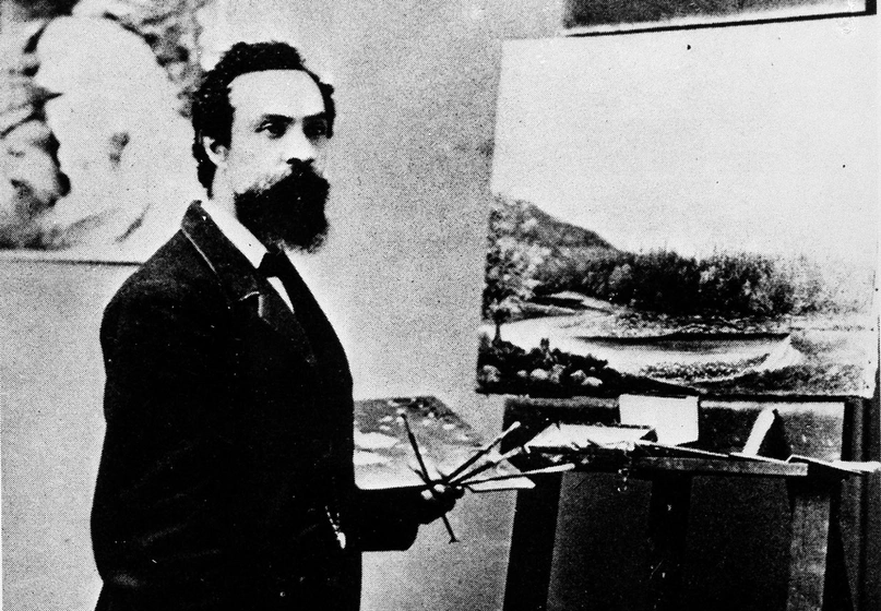 A black-and-white photo of a man in a suit, holding a palette and brushes in front of an easel.