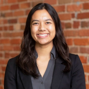 A smiling person against a brick background.