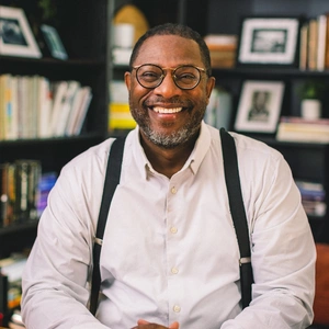  A smiling person in a white shirt and black suspenders, in an office.