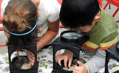 two young children looking through magnifying glasses at soil