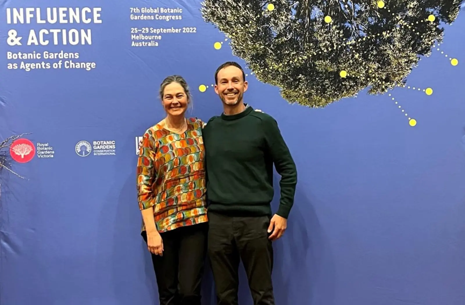 Nicole Cavender and Sean Lahmeyer stand in front of a sign that says, "Influence and Action: Botanic Gardens as Agents of Change."