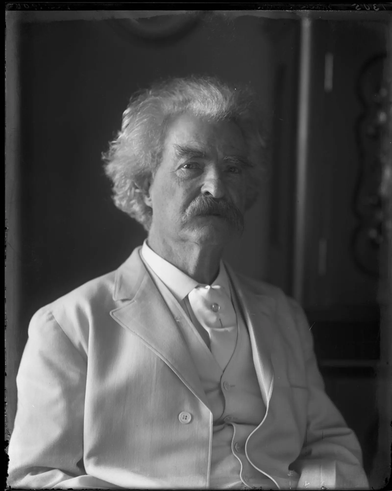 Black-and-white photo of Mark Twain, partially in shadow.
