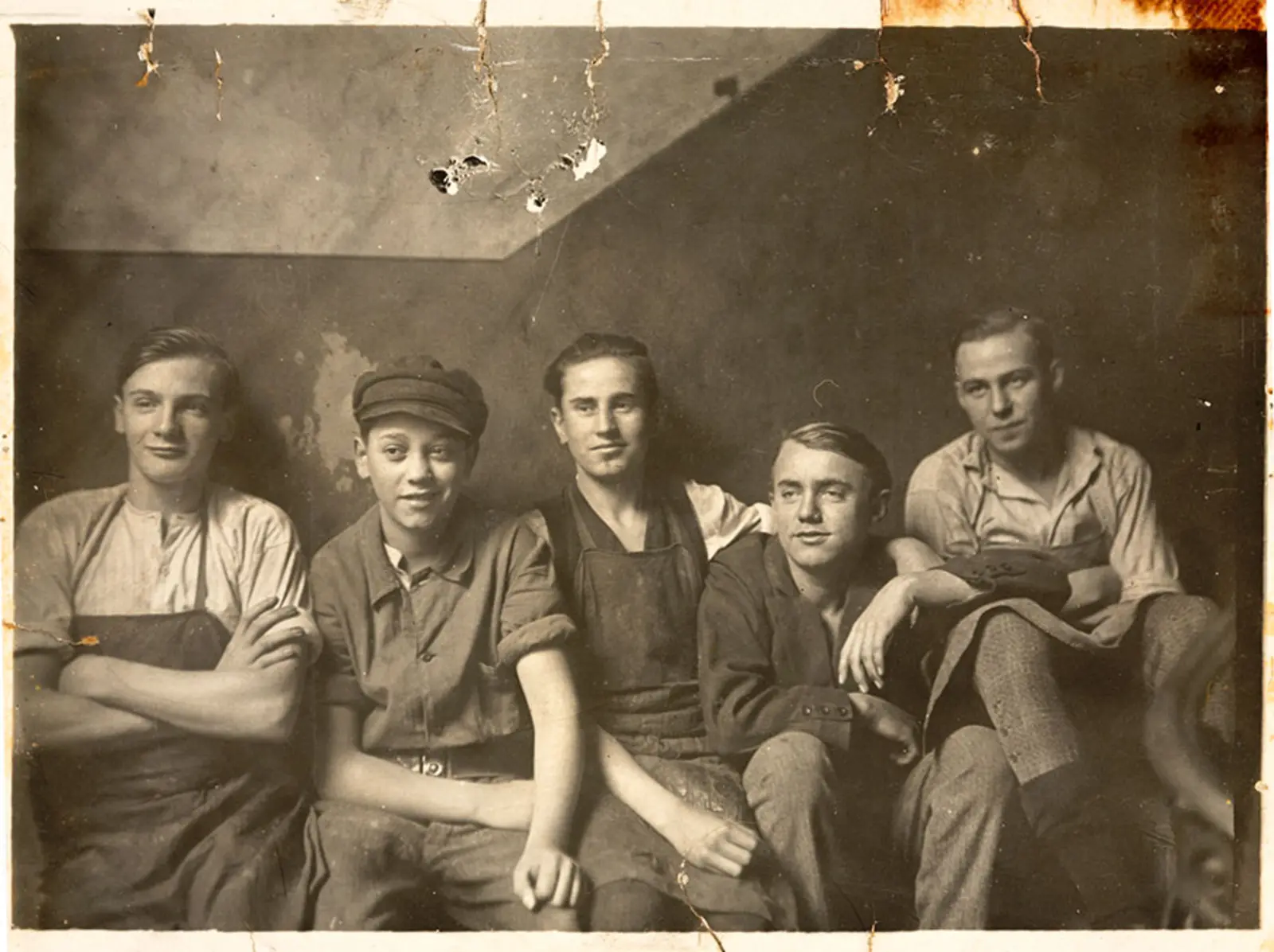 Black-and-white photo of five young men sitting against a wall.