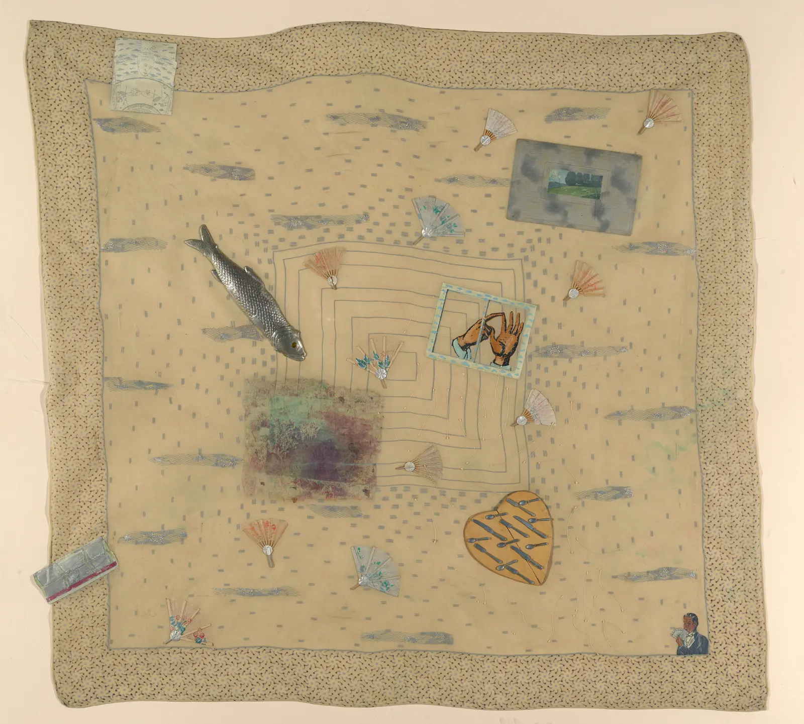 mixed media assemblage artwork on a beige handkerchief featuring an assortment of small items including a heart filled with small metal spoons and knives, small hands inside a window, small fans, a fish, a magician, and pieces of gray blue lace.