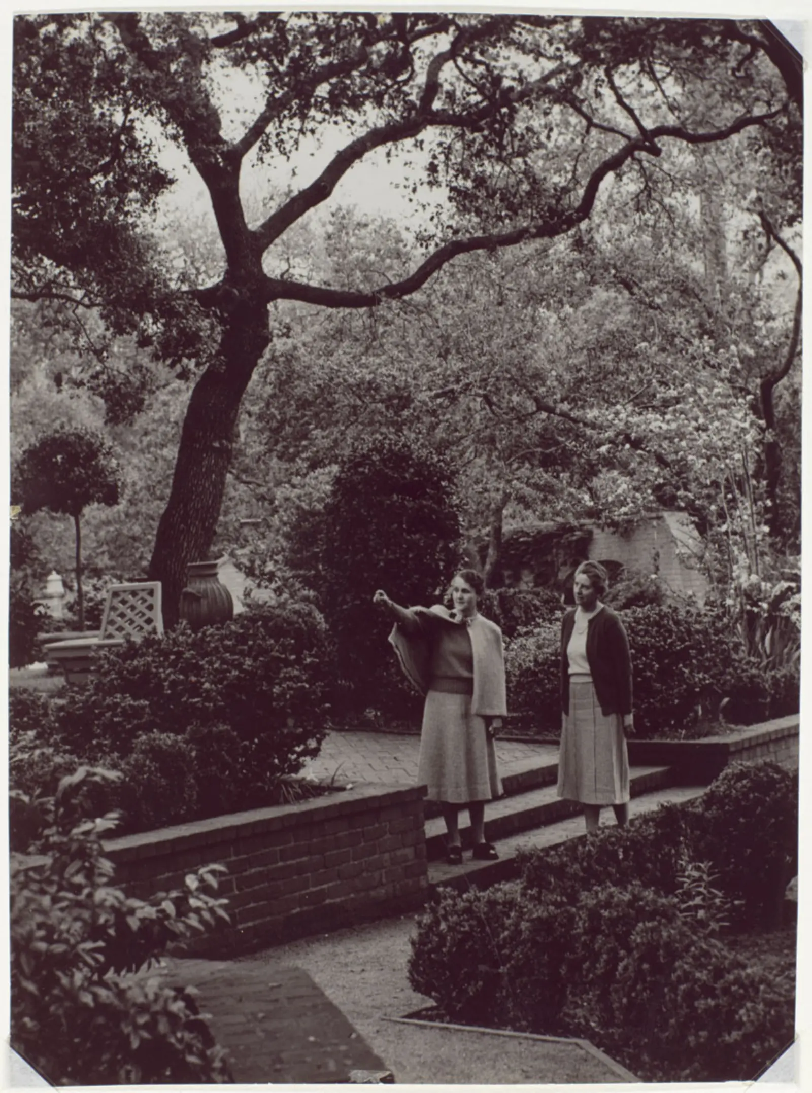 A grayscale photo of two people in a mature garden.