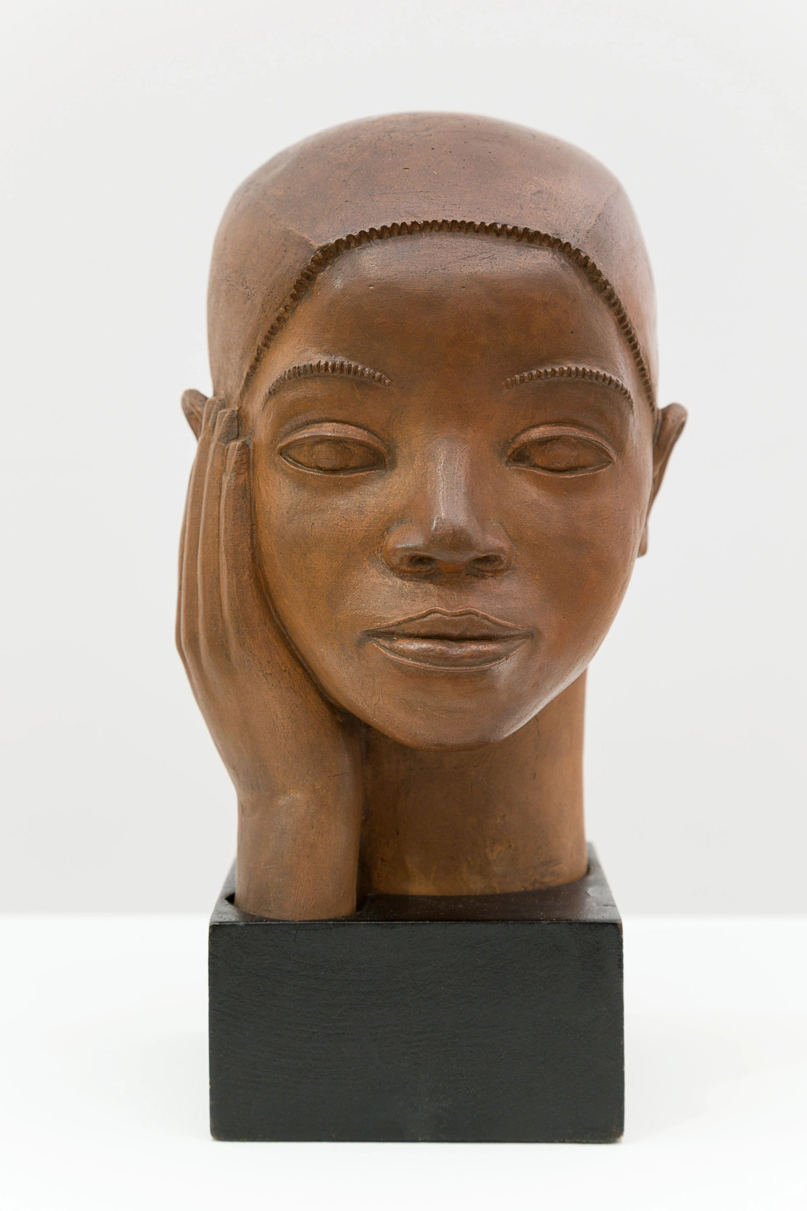 terracotta head of a young Black person with a calm expression and a hand touching its cheek on a black block