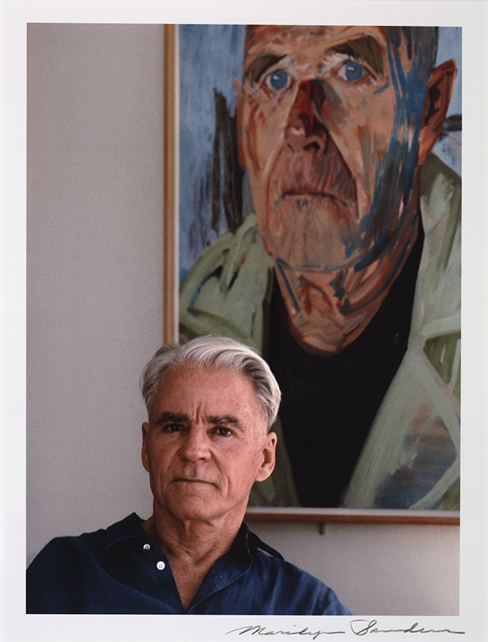 Don Bachardy in 1991, posing in front of his portrait of novelist Christopher Isherwood (1983). Photo by Marilyn Sanders, reproduced by permission. The Huntington Library, Art Collections, and Botanical Gardens.