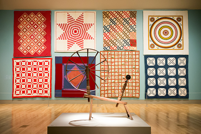 This selection of quilts, made between 1850 and 1900, includes a wide variety of styles and patterns. The spinning wheel in the foreground dates from the early 18th century. Jonathan and Karin Fielding Collection. Photo by Kate Lain. 