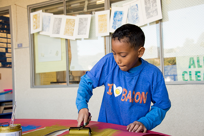 Nicanor Taylor, another student in Pam Chirichigno’s fifth-grade class, focuses on getting just enough ink onto the roller. Behind him are examples of prints by other students. Photo by Kate Lain.