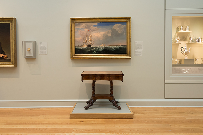 The mahogany Card Table is displayed beneath Sailing Ships off the New England Coast, circa 1855, by Fitz Henry Lane. Card Table, mid 19th Century. Unknown maker, American. Mahogany with satinwood and holly inlay, 29 3/8 x 34 x 18 5/8 in. (74.6 x 86.4 x 47.3 cm.). The Huntington Library, Art Collections, and Botanical Gardens. Photo by Kate Lain.