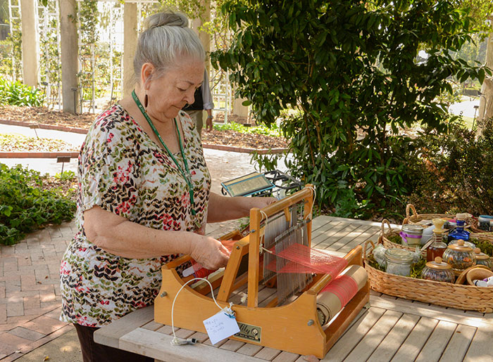 Lorynne Young, Herb Garden docent chair, weaves on a table loom in the Herb Garden. Photo by Deborah Miller.